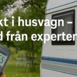 En hand håller en fuktmätare som visar 16,5 % framför en vit husvagn på en grön campingplats. Texten ”Fukt i husvagn – råd från experten” syns över bilden.